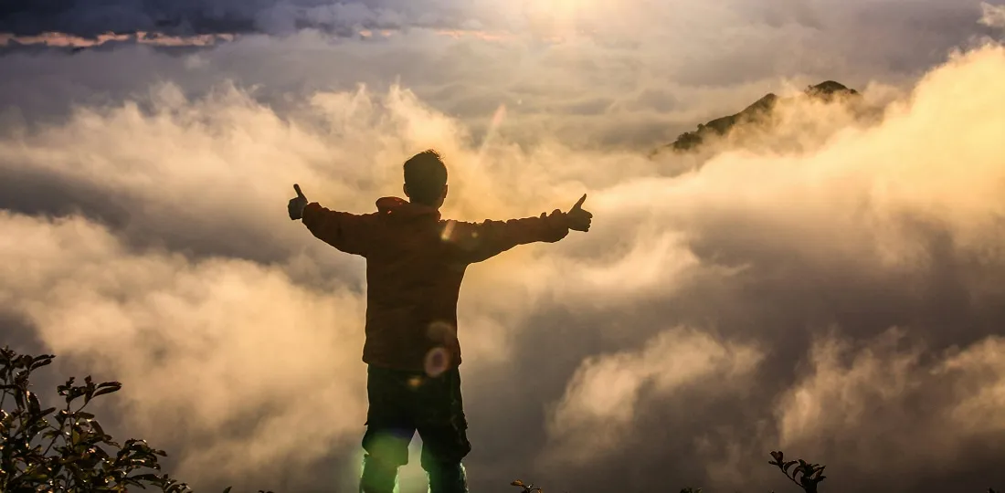 Wanderer über dem Wolkenmeer bei Sonnenaufgang auf einem Berggipfel